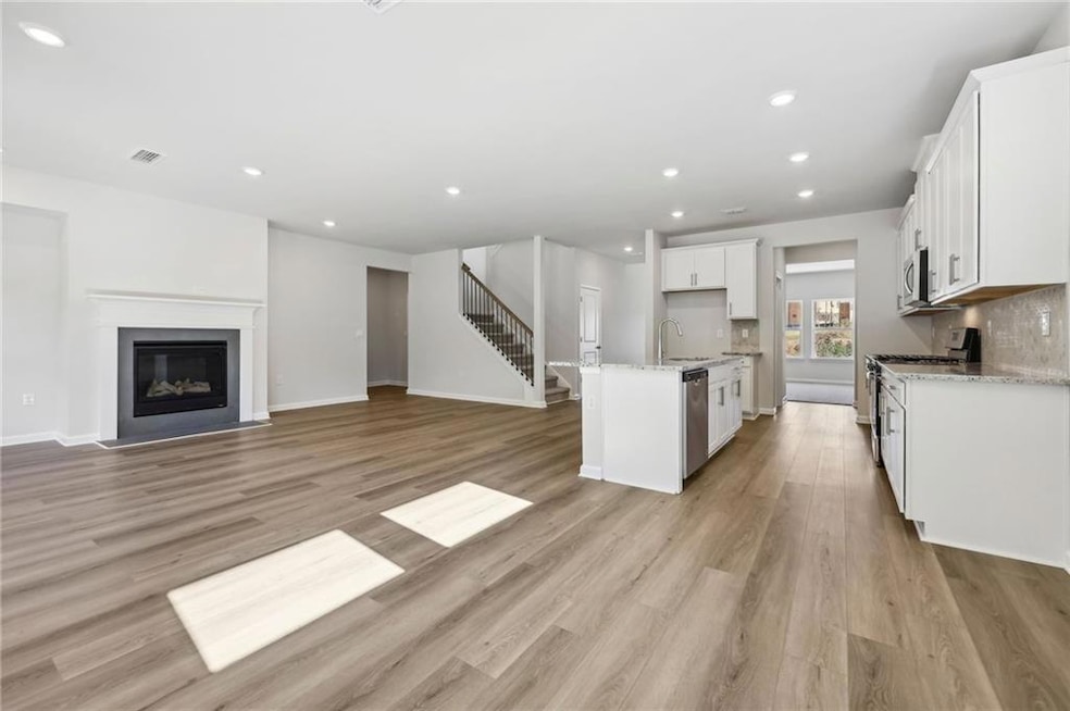 Kitchen with appliances with stainless steel finishes, open floor plan, light stone countertops, white cabinets, and light wood finished floors