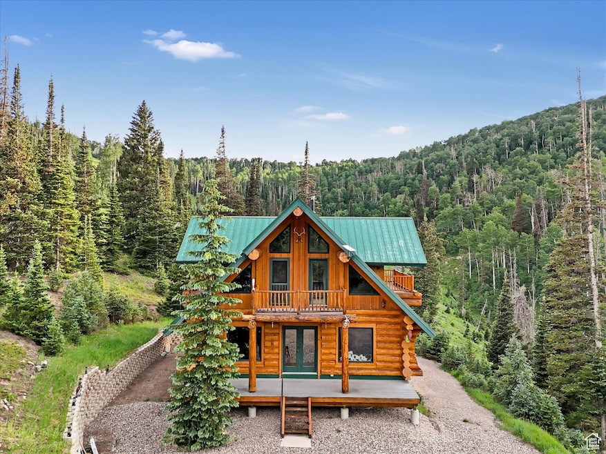 Back of property featuring a forest view, a porch, french doors, log exterior, and a metal roof