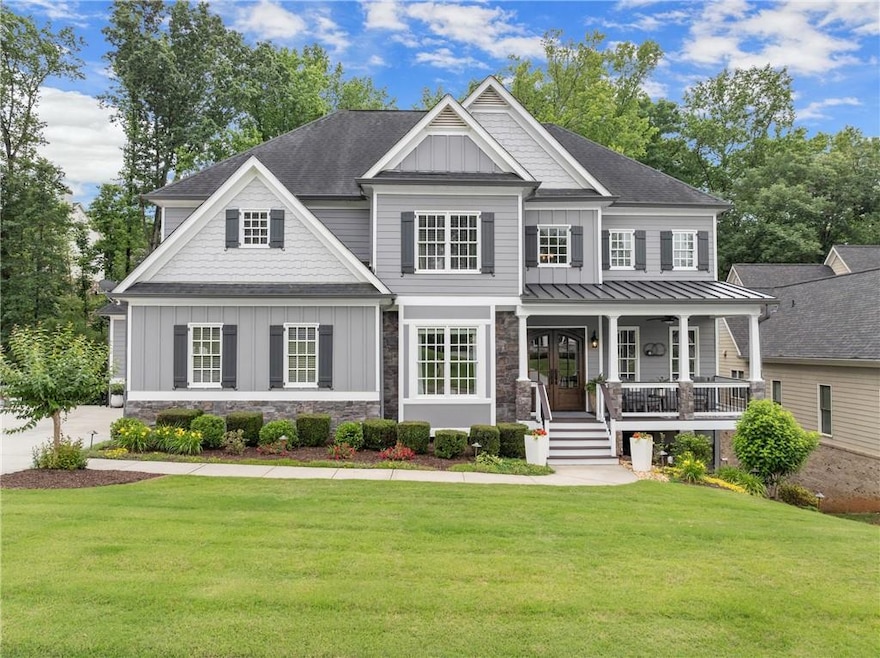 Craftsman-style home with board and batten siding, covered porch, a front yard, stone siding, and roof with shingles