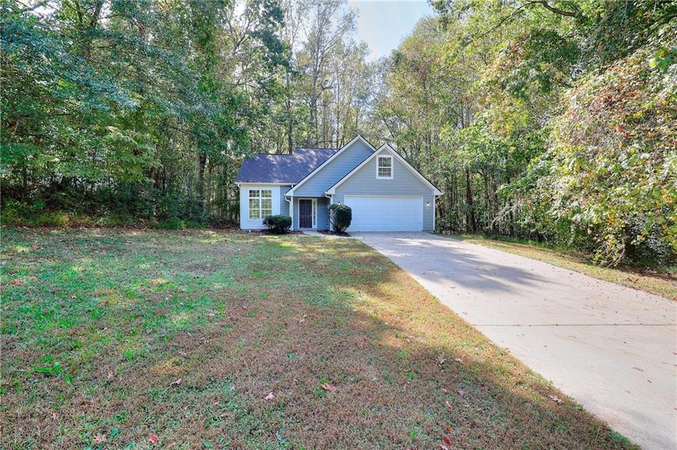 View of front facade featuring concrete driveway, a front lawn, and a wooded view