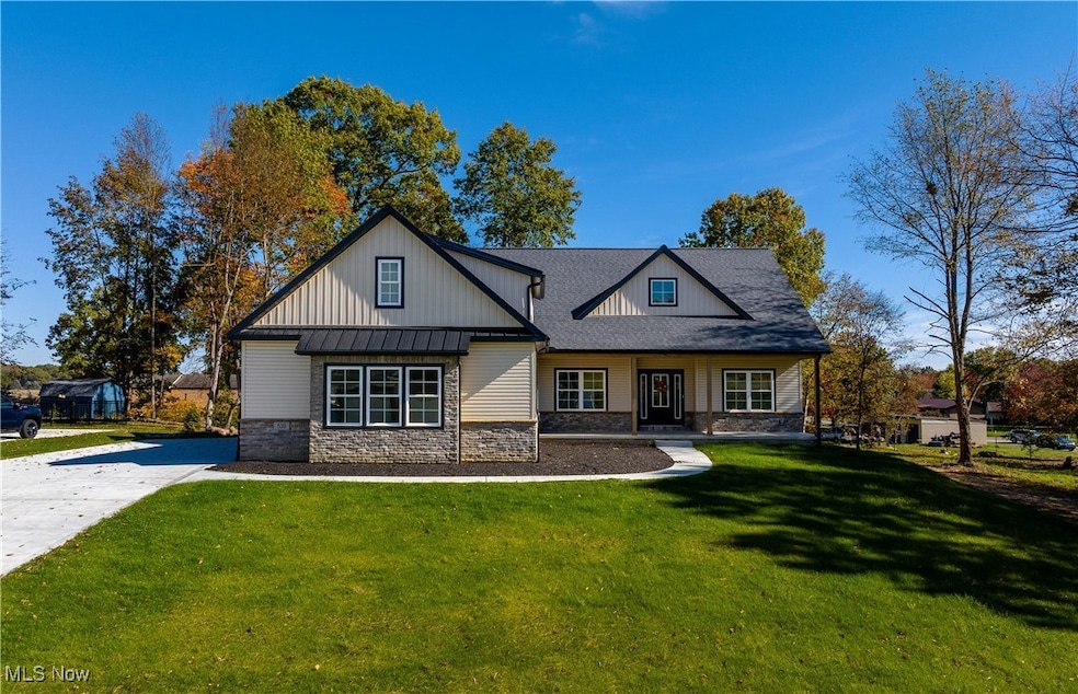 View of front facade featuring a front yard, a porch, stone siding, and roof with shingles