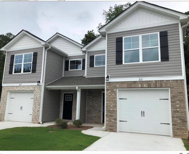 View of front of home featuring brick siding, an attached garage, concrete driveway, covered porch, and a front lawn