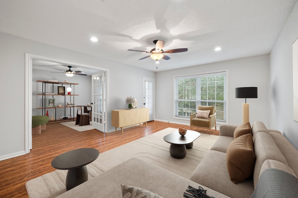 Bright living area with large windows and open layout, flowing into an adjoining study through French doors. Virtually staged to highlight the room’s size, flexibility, and potential.