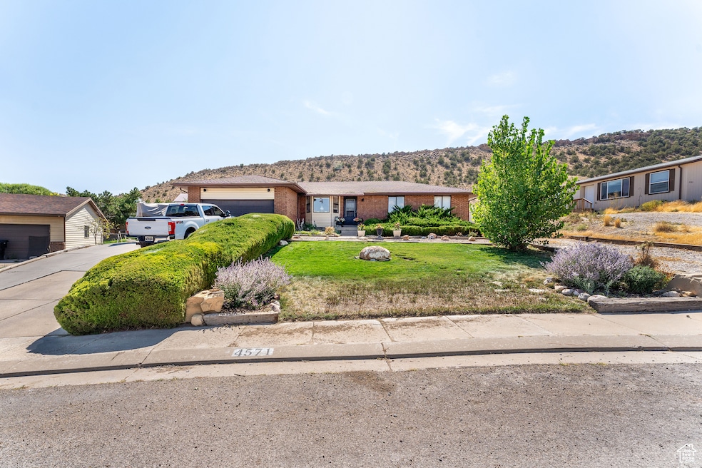 View of front of home with driveway, a front yard, brick siding, an attached garage, and a mountain view