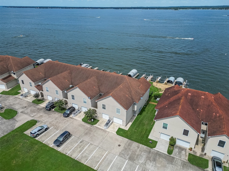 This photo showcases a row of waterfront townhouses with red-tiled roofs, each featuring attached garages. The properties offer direct access to a large body of water with private docks. Ample parking and well-maintained lawns are visible, providing a scenic and convenient living environment.