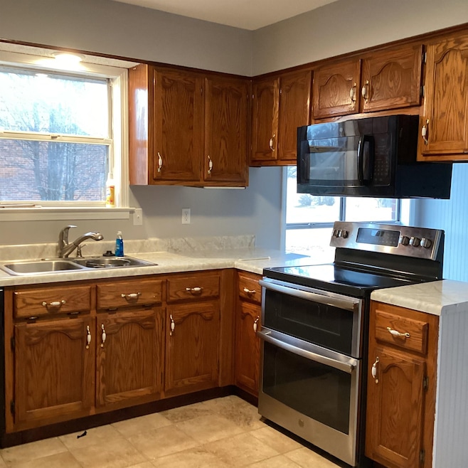 Kitchen with range with two ovens, black microwave, a sink, light countertops, and brown cabinets