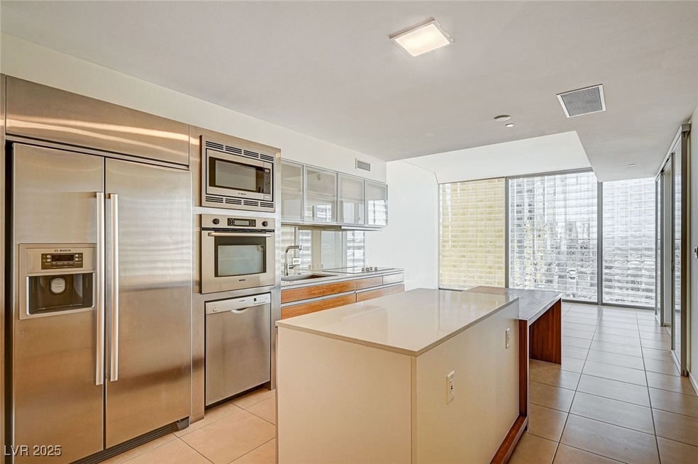 Kitchen featuring built in appliances, a kitchen island, floor to ceiling windows, light tile patterned floors, and glass insert cabinets