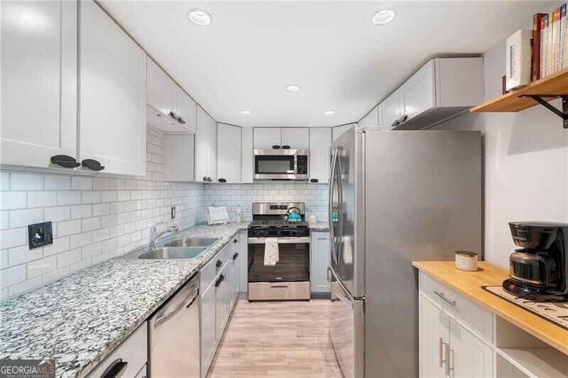 Kitchen with white cabinetry, appliances with stai