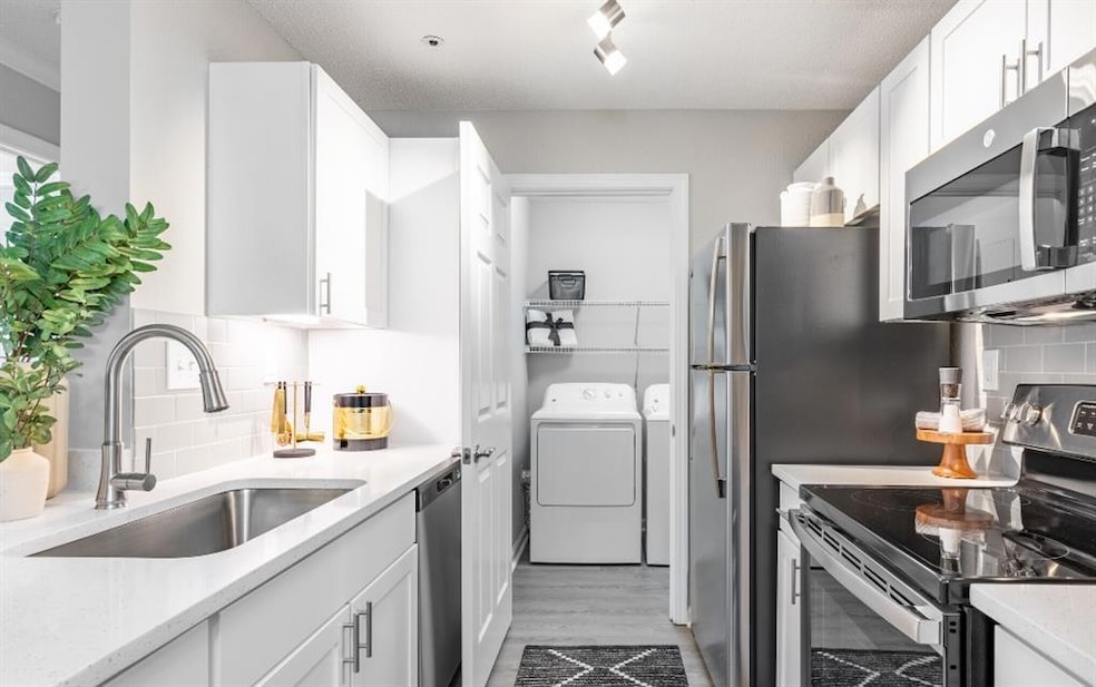 Kitchen with tasteful backsplash, light hardwood / wood-style flooring, appliances with stainless steel finishes, and sink