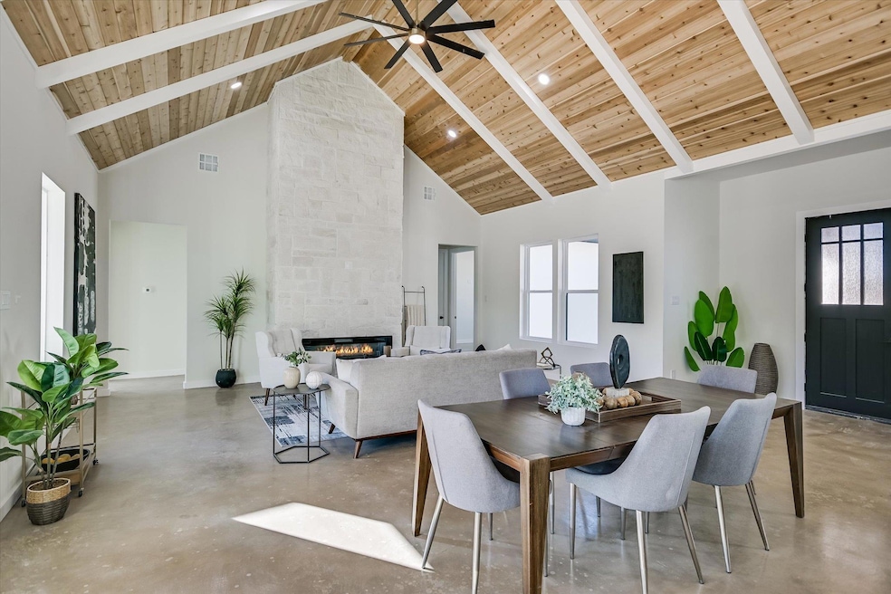 Dining space featuring concrete floors, high vaulted ceiling, a fireplace, a wood ceiling with exposed beams, and a ceiling fan