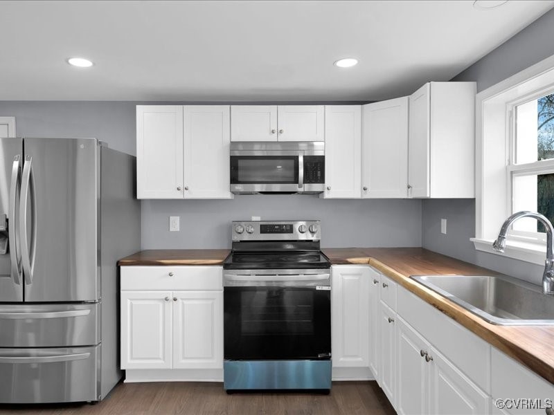 Kitchen with stainless steel appliances, butcher block counters, sink, and white cabinetry