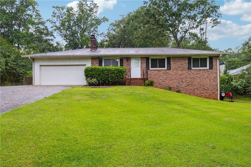 Ranch-style house featuring driveway, a front yard, a garage, a chimney, and brick siding