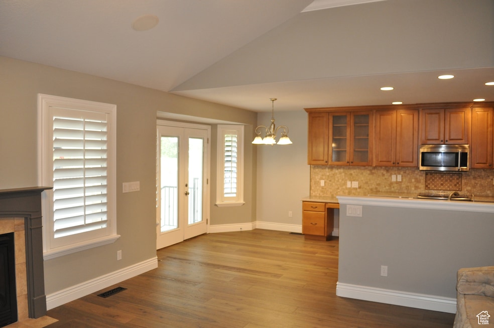 Kitchen featuring brown cabinetry, recessed lighting, stainless steel microwave, decorative backsplash, and hanging light fixtures