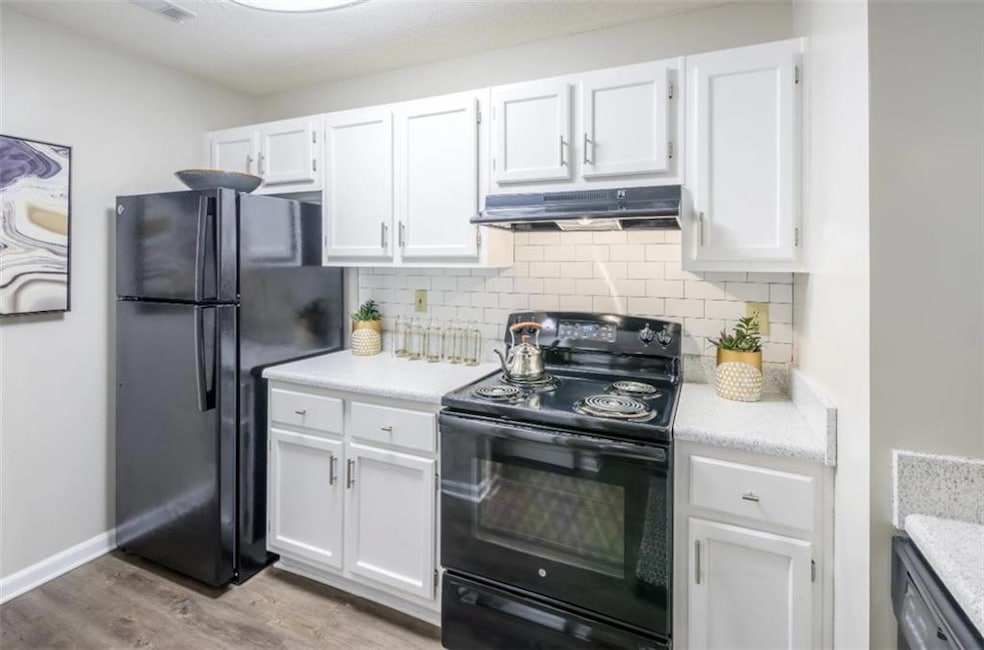 Kitchen with light hardwood / wood-style flooring, black appliances, white cabinetry, and decorative backsplash
