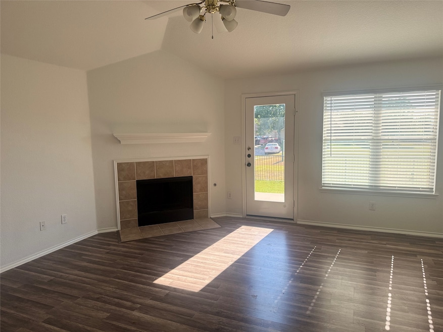 Unfurnished living room with dark wood-style flooring, a tiled fireplace, and ceiling fan