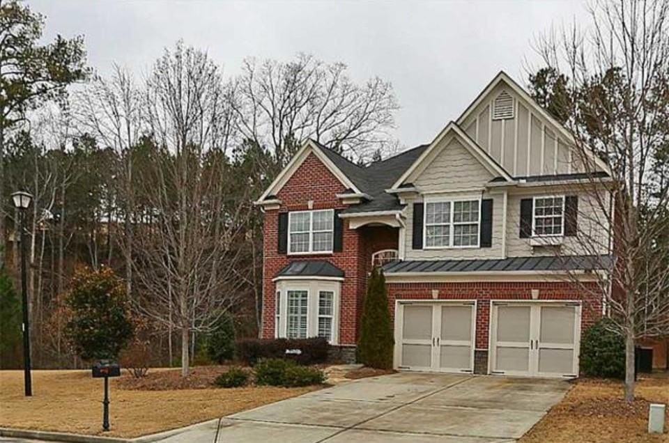 View of front of house with driveway, a standing seam roof, a garage, brick siding, and a metal roof