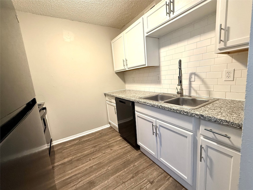 Kitchen with freestanding refrigerator, dark wood-style floors, backsplash, dishwasher, and white cabinets