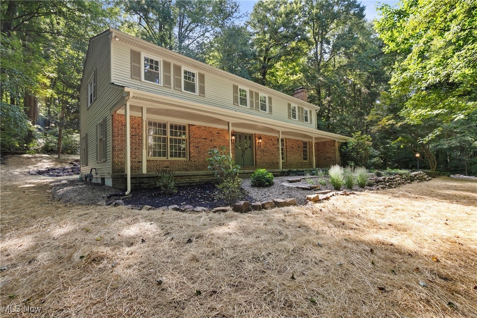 Traditional home featuring a chimney, brick siding, a porch, and view of wooded​​‌​​​​‌​​‌‌​​​‌​​‌‌​​‌‌​‌​​​‌‌​​‌​​​​​‌ area