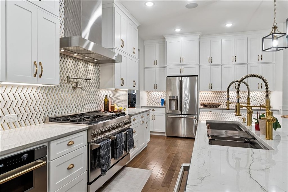 Kitchen with high quality appliances, wall chimney exhaust hood, white cabinets, backsplash, and recessed lighting