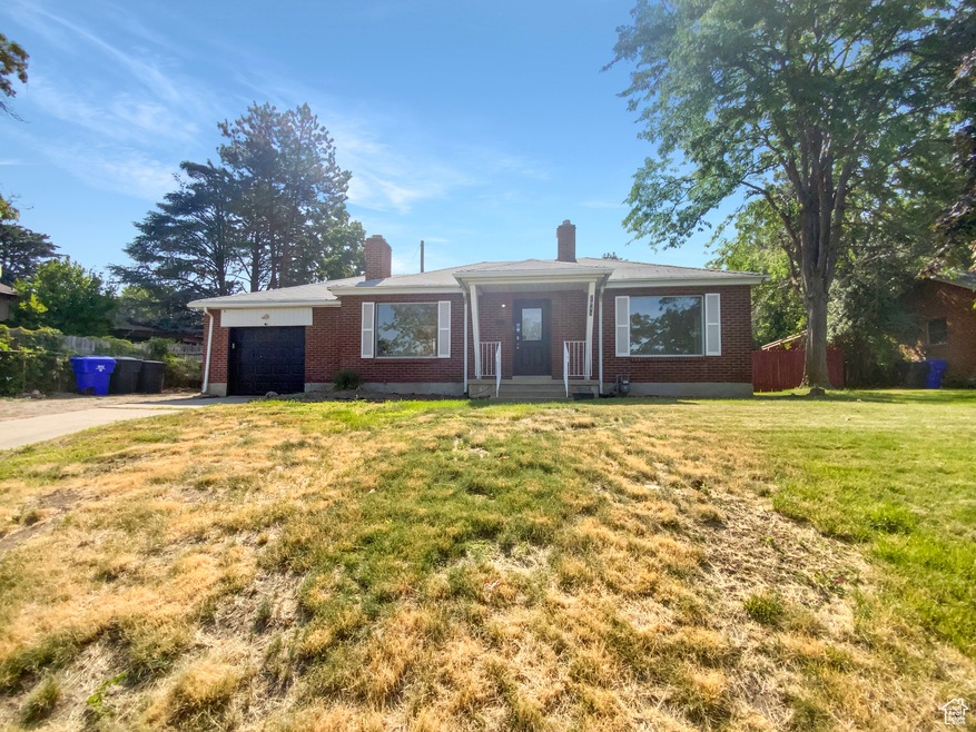 Ranch-style home featuring brick siding, a chimney, a garage, concrete driveway, and a front yard