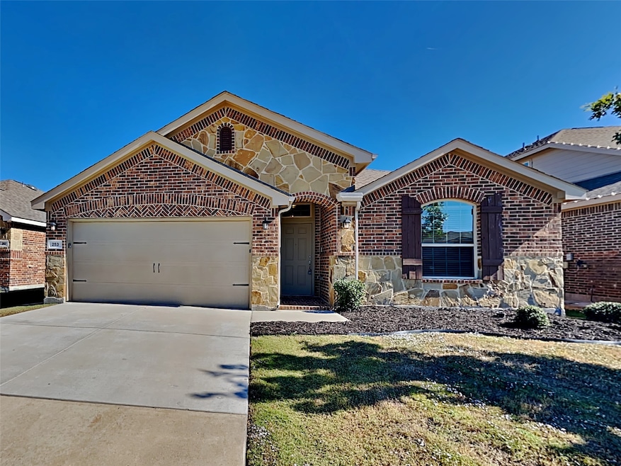 View of front of property featuring stone siding, concrete driveway, a garage, brick siding, and a front yard