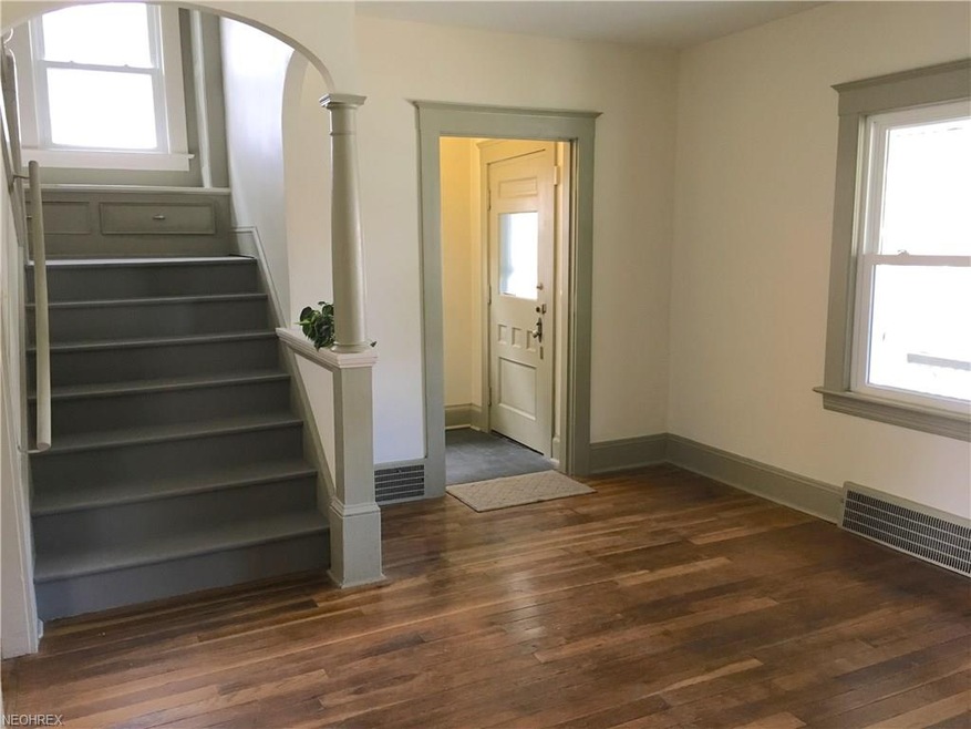 A view of the living room looking toward the vestibule and staircase with cozy window seat. Original Hardwood floors.