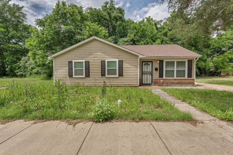View of front of property with brick siding, a shingled roof, and view of wooded area