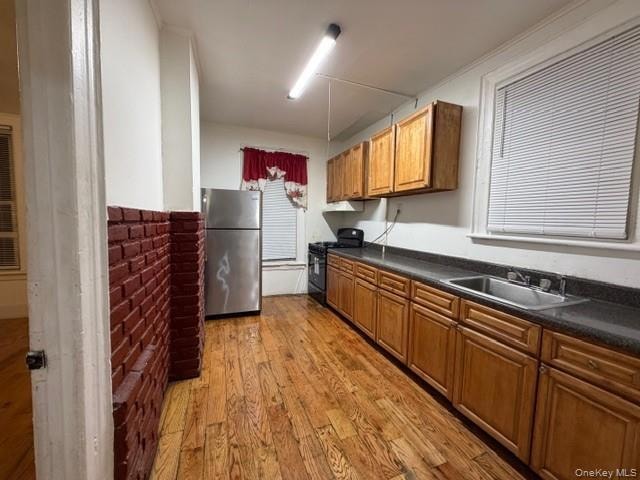 Kitchen with dark countertops, dark wood-style floors, brown cabinetry, freestanding refrigerator, and black gas range