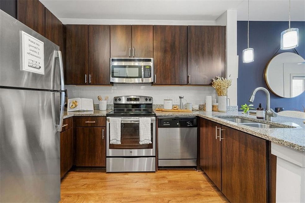 Kitchen with stainless steel appliances, light hardwood / wood-style floors, sink, light stone countertops, and hanging light fixtures