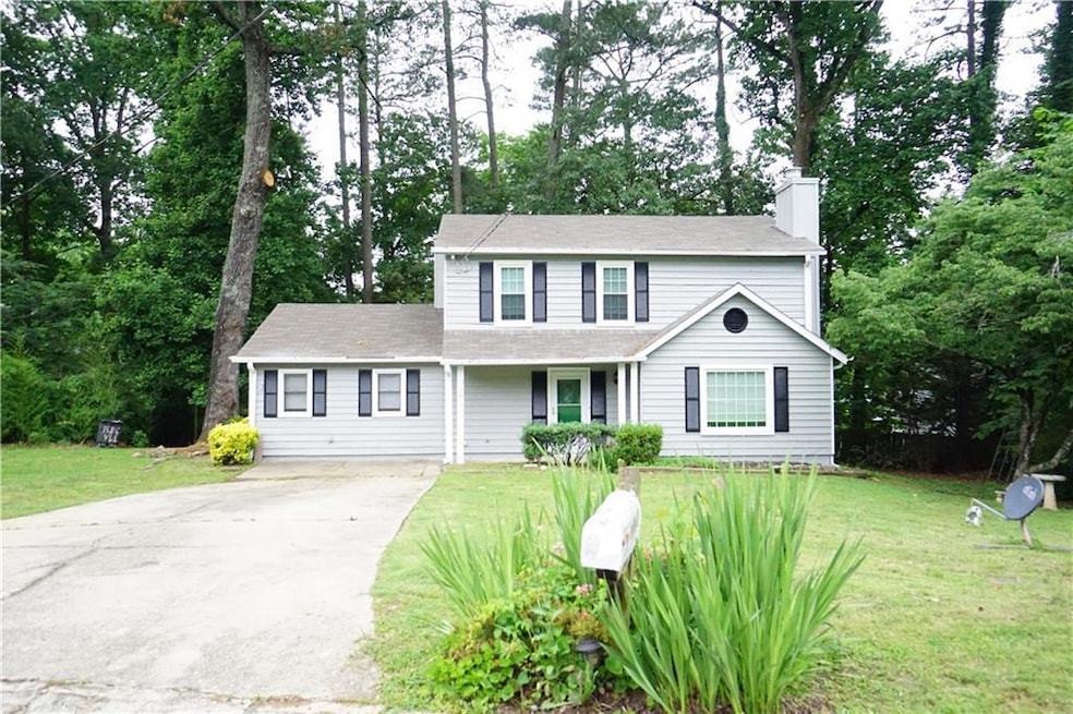 Traditional home featuring concrete driveway, a chimney, a front yard, and view of wooded area