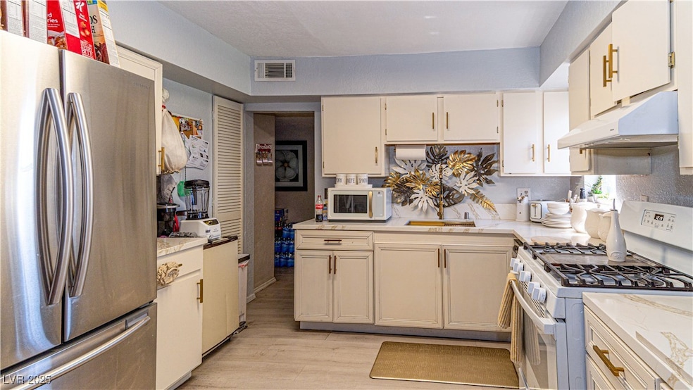 Kitchen with white appliances, under cabinet range hood, light wood-style floors, and light stone counters