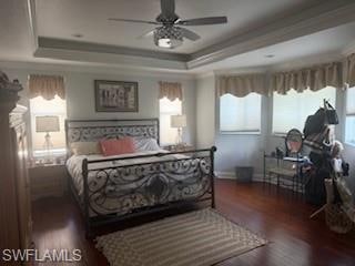 Bedroom featuring dark wood-type flooring, a tray ceiling, and a ceiling fan
