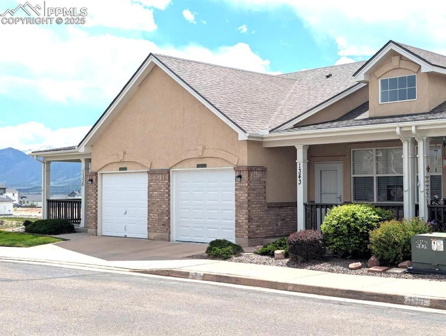View of front of house with driveway, mountains behind, a garage, brick siding, and stucco siding
