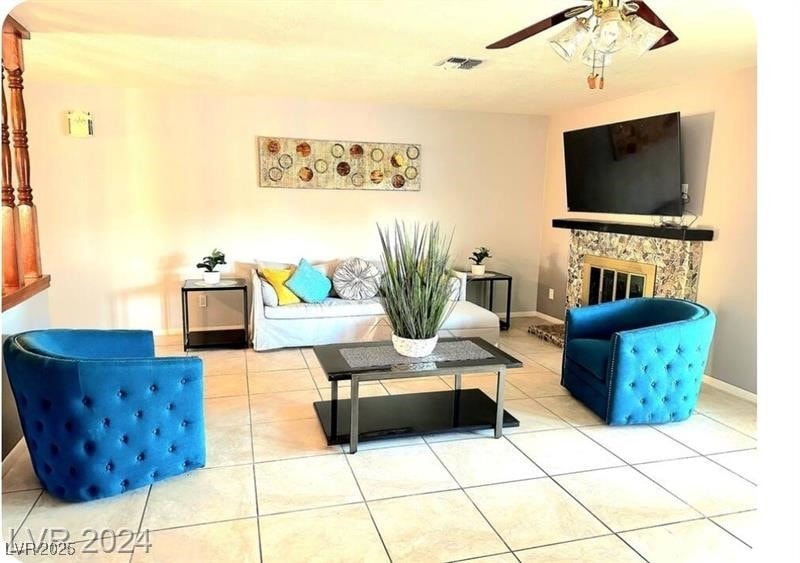 Tiled living room with a glass covered fireplace and ceiling fan