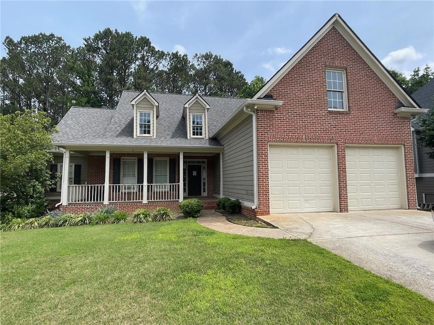 View of front of house with a porch, driveway, brick siding, a front yard, and an attached garage