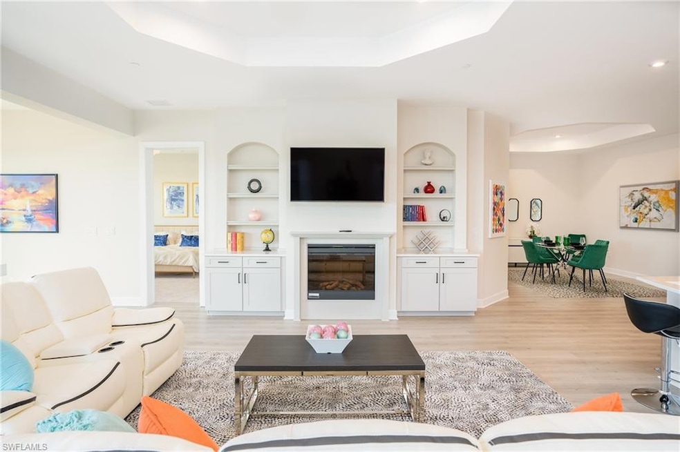 Living area featuring a raised ceiling, built in features, light wood-style flooring, a glass covered fireplace, and recessed lighting