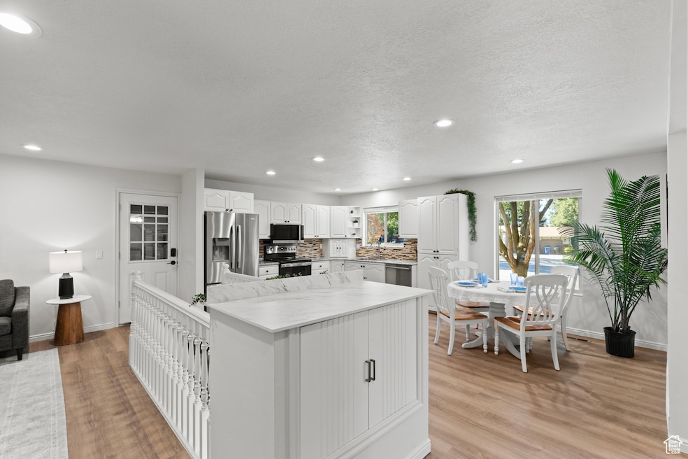 Kitchen featuring white cabinets, stainless steel appliances, decorative backsplash, recessed lighting, and a kitchen island