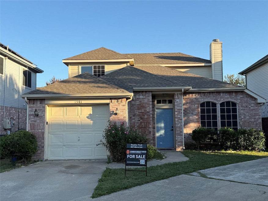 Traditional-style house featuring roof with shingles, concrete driveway, brick siding, a garage, and a chimney
