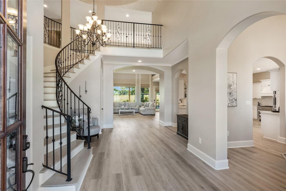 Step inside to a light-filled foyer featuring soaring ceilings, a graceful curved staircase, and wide-plank flooring. The open flow leads seamlessly into the main living space, creating an inviting layout for everyday living and entertaining.