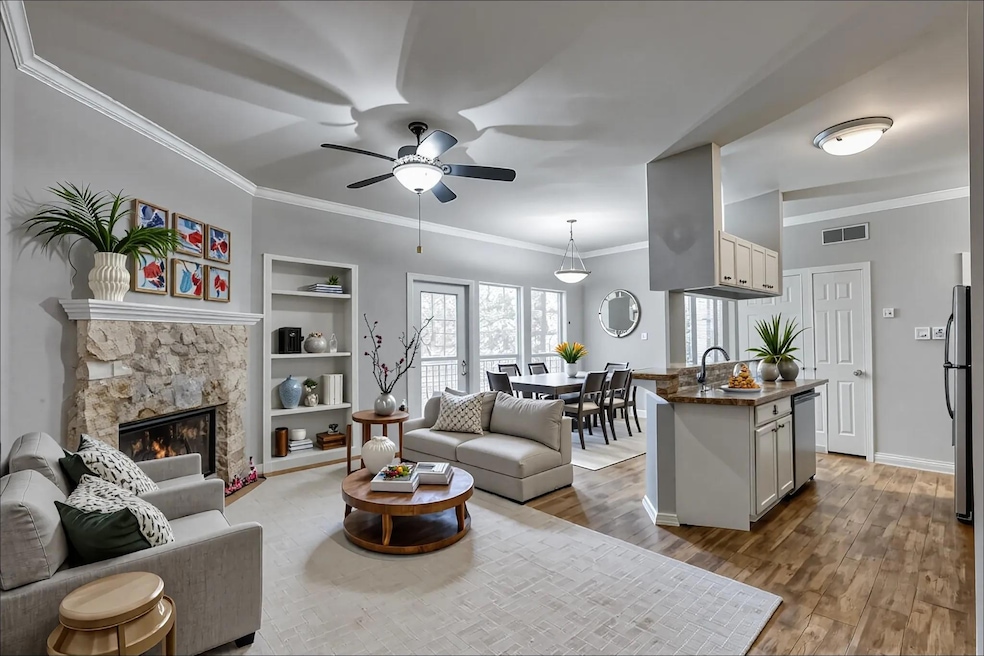 Living room featuring crown molding, a fireplace, built in features, wood finished floors, and ceiling fan