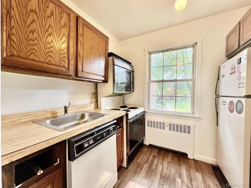 Kitchen featuring white appliances, radiator heating unit, light wood-style floors, and light countertops