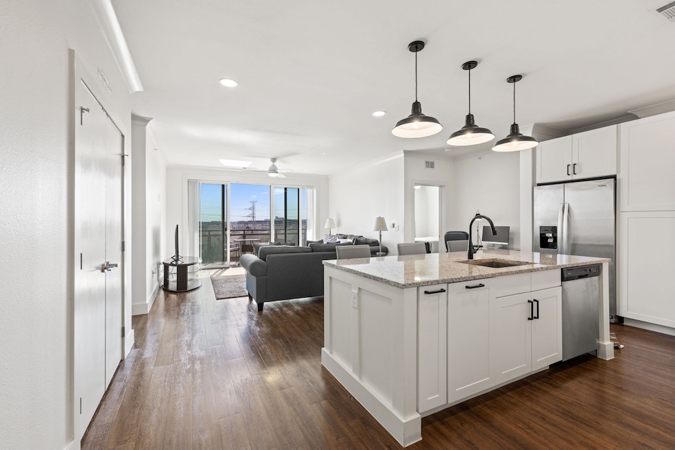 Kitchen with white cabinets, hanging light fixtures, a center island with sink, light stone countertops, and recessed lighting