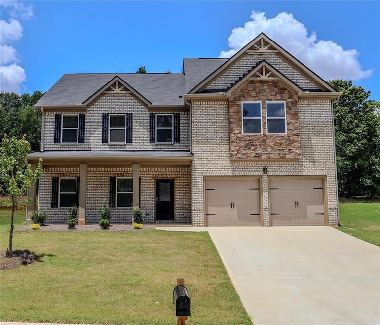 View of front facade featuring covered porch, an attached garage, a front lawn, driveway, and brick siding