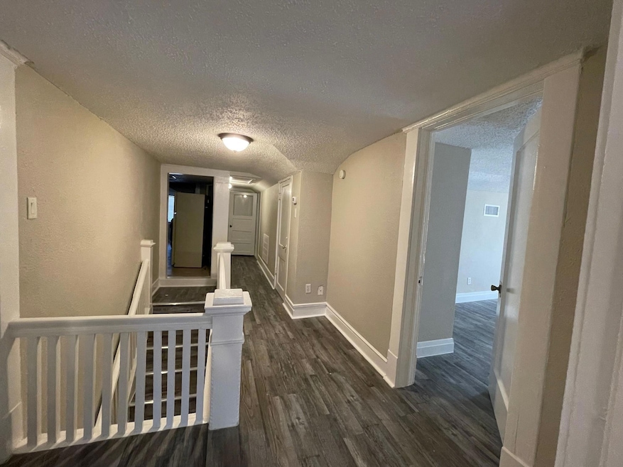 Hallway with a textured ceiling, baseboards, and d