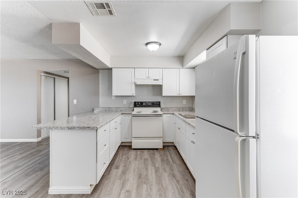 Kitchen with white appliances, a peninsula, light countertops, white cabinetry, and light wood-style flooring