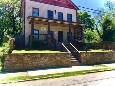 View of front of property featuring covered porch, stairway, and a fenced front yard