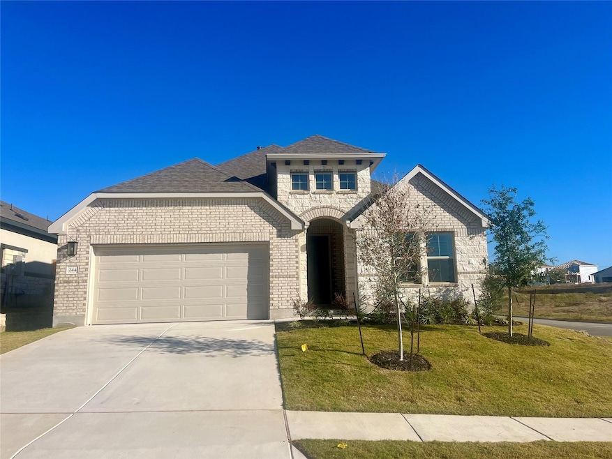 French country inspired facade with brick siding, a front lawn, a garage, and concrete driveway