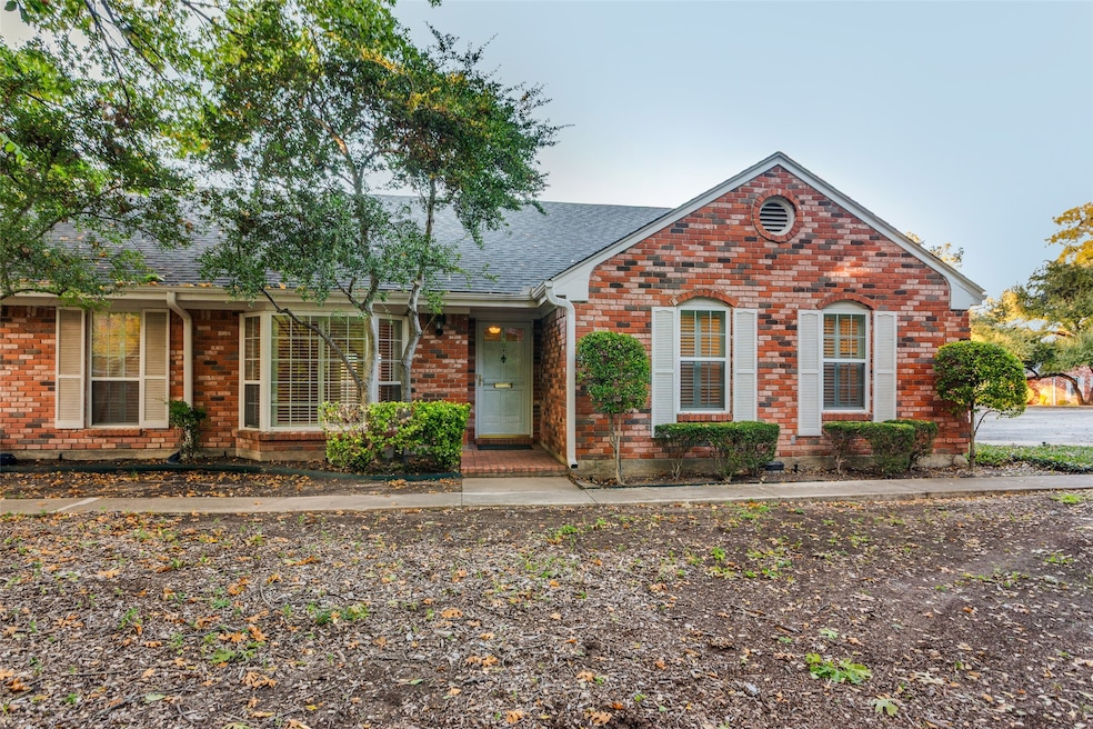 View of front of property with a shingled roof and brick siding. Corner unit, park-like front yard with creek.