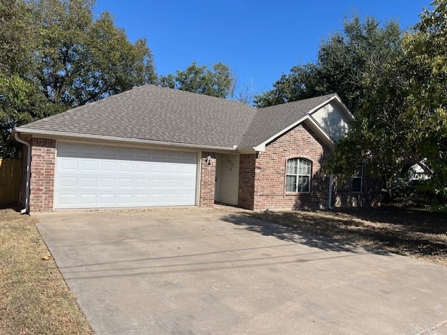 Ranch-style house featuring brick siding, driveway, a shingled roof, and a garage