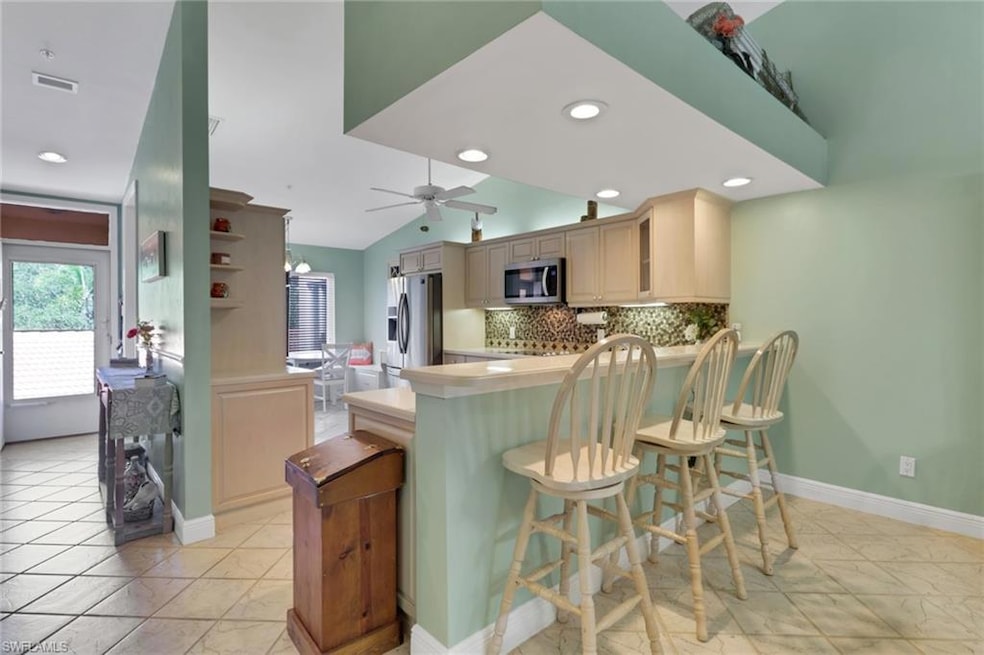 Kitchen with tasteful backsplash, a kitchen breakfast bar, stainless steel appliances, light countertops, and lofted ceiling